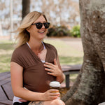 Woman sitting on a park bench holding a coffee cup, wearing sunglasses and a brown top.